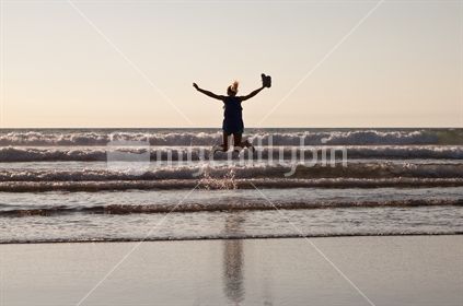 A girl jumping over waves at sunset