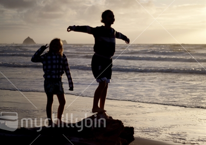 Two kiwi girls 
silhouetted against the sea at sunset.
