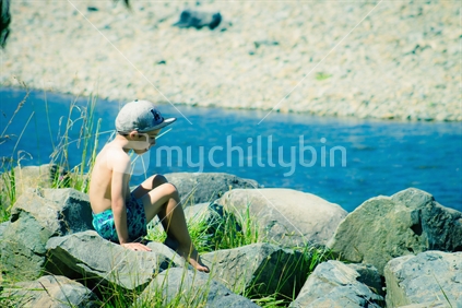 Young Boy sitting on rocks at a river in summer