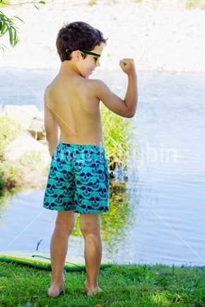 Young Boy beside a river in his swimming trunks in summer