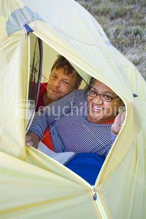 Middle aged tramping couple peer through opening in yellow tent