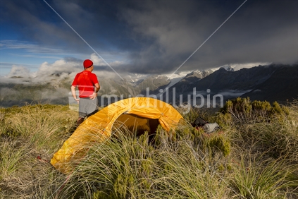 Red male camper looks out toward Fox Glacier, from top of Mount Fox, Westland National Park