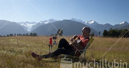 Freedom camper strums guitar sitting in beach chair at Fox River flats, South Westland