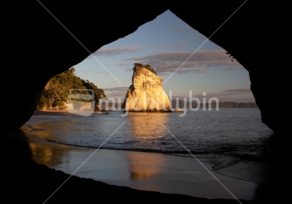 Framed by the iconic seacave at Cathedral Cove, Te Hoho Rocks is reflected in wet sand