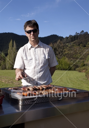 New Zealand bloke frying sausages on a barbeque