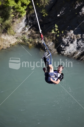 Young man bungee jumper above Kawerau River, on the rebound after a dunking, near Queenstown