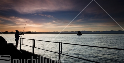 Silhouette of yong woman fishing off Rocks Road at sundown, Nelson