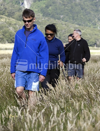 Four trampers walk grassy river flats in Mt Aspiring National Park, Otago