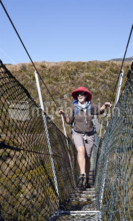 Middle-aged lady crosses swing bridge on Heaphy Track, Kahurangi National Park