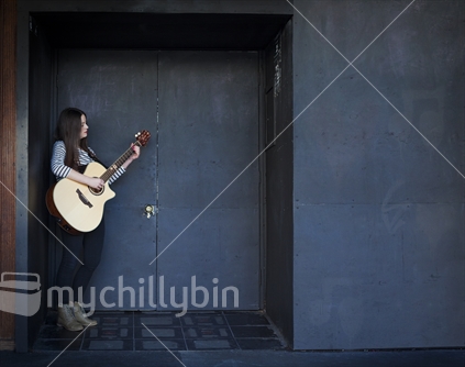 Attractive teenage girl strums guitar in dark doorway of night club