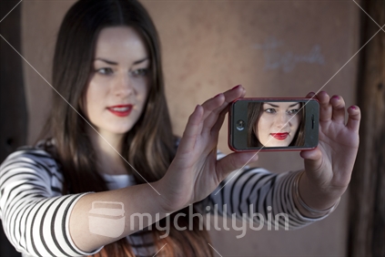 Teenage girl takes her self-portrait with smart phone (focus phone image)