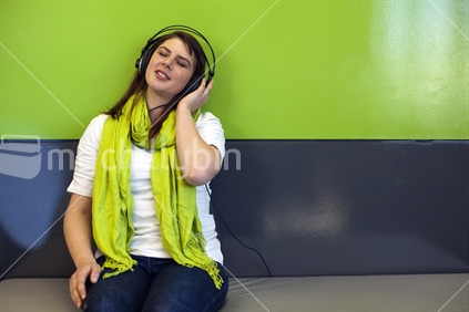 Young woman in jeans and lime green scarf listens to music on headphones