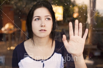 Teenage girl peers outside through window with raindrops