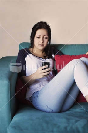 Teenage girl text messaging on a cellular phone sitting on sofa