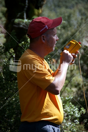 Tramper dressed in yellow uses a mountain radio to get a weather forecast.