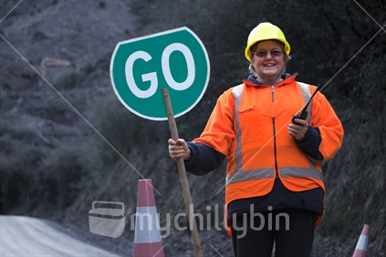Happy Go Lucky - Lady traffic controller on rural road with large GO sign & radio