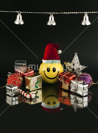 Happy Christmas - yellow smiley face ball wearing Santa hat amongst miniature gifts