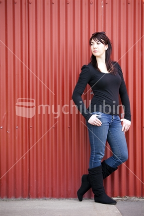 Brunette young woman leans against red colour steel wall