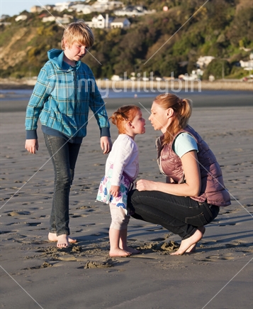 Eye to eye; Solo mum with her two children on a sandy beach