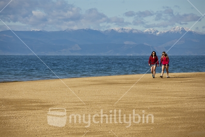 Two girlfriends tramp along golden sand on the Abel Tasman coastal track.