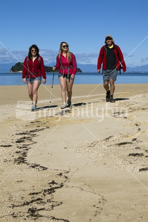 Three hiking friends walk the golden sands of Abel Tasman National Park.