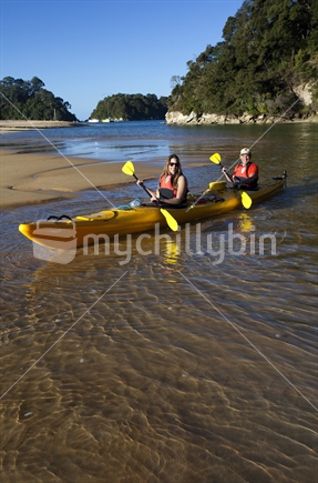 Couple paddle a kayak into the idyllic waters of Kaiteriteri Beach.
