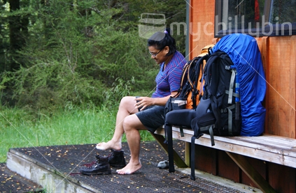 Pack loaded and ready to go (focus), with Polynesian woman putting boots on beyond; West Sabine Hut, Nelson Lakes National Park.