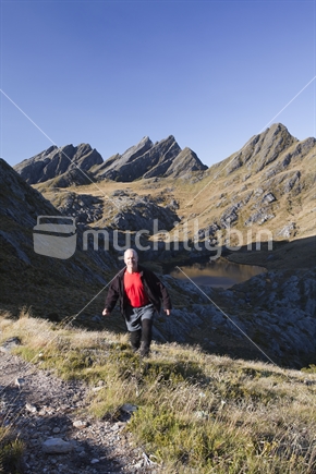 Solo hiker departs Adelaide Tarn, deep in the heart of Kahurangi National Park. The rugged Dragons Teeth are beyond.