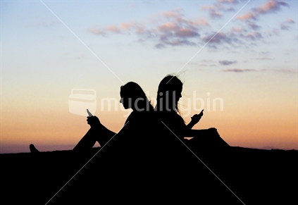 Two 18-year-old girls text one another - sunset silhouette