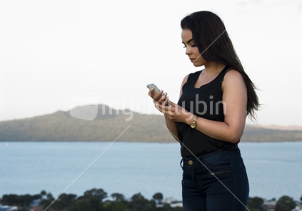 18-year-old girl on cellphone with Auckland's Rangitoto Island beyond 