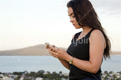 18-year-old girl on cellphone with Rangitoto Island beyond