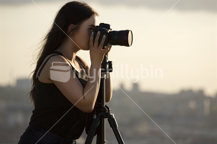 Young woman photographer with camera on tripod - profile view, close up with dusk light