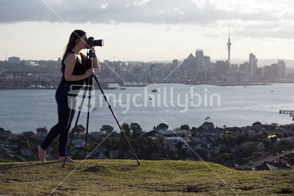 Person with camera on tripod - profile view with Auckland City skyline beyond