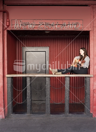 Beautiful female busker strums guitar outside nightclub