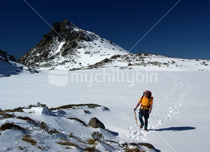 Alpine tramper walks across a frozen Iron Lake, Kahurangi National Park