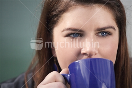 Closeup of woman's face sipping from blue mug