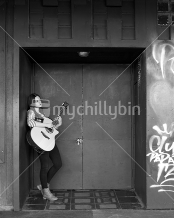 Female busker strums guitar outside nightclub