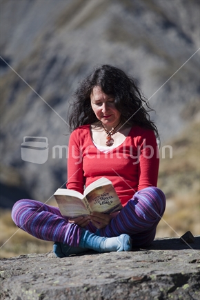 Middle-aged brunette reads a novel in red and purple polyprop tramper's clothes