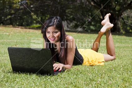 Attractive young Asian lady in Auckland Domain using her laptop computer