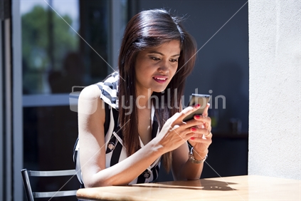 Young Asian woman eagerly uses cellphone in urban cafe