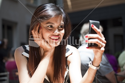 Happy young lady smiles at her smart phone in a crowded cafe