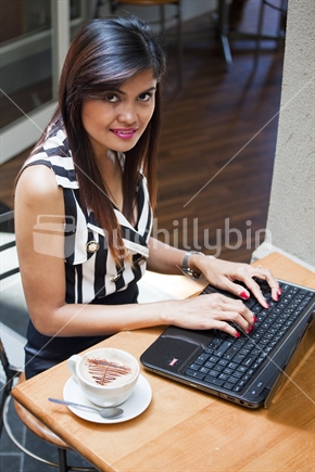 Modern, chic woman works on laptop computer at a busy city cafe