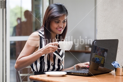 Attractive young Asian woman drinks coffee while working on the go