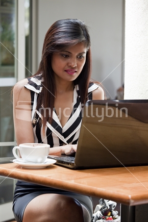 Good-looking Asian woman types message on laptop computer in urban cafe