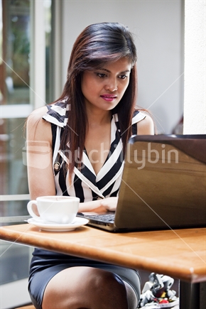 Attractive Asian brunette types message on laptop computer in urban cafe