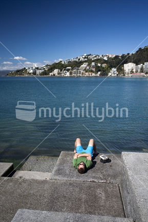 Kiwi bloke sunbathes on pier at Oriental Bay, Wellington