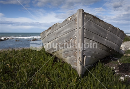 Old wooden boat on grass beside Pacific Ocean. Bow view.