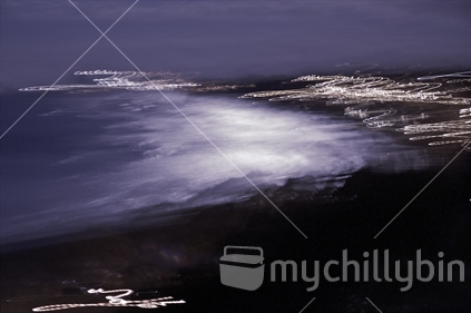 Oakura Beach, Taranaki at high tide bathed in the light of a full moon with surrounding street lights at play.