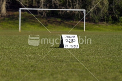 Ground closed sign in front of soccer goal post's that are out of focus