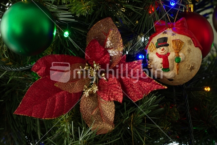 Christmas pionsetta decoration on a tree with snowman bauble in the background
